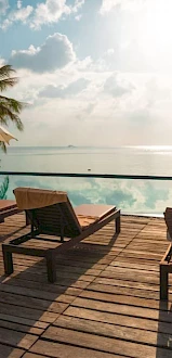 A serene tropical scene with lounge chairs and umbrellas on a wooden deck overlooking a calm sea under a blue sky.