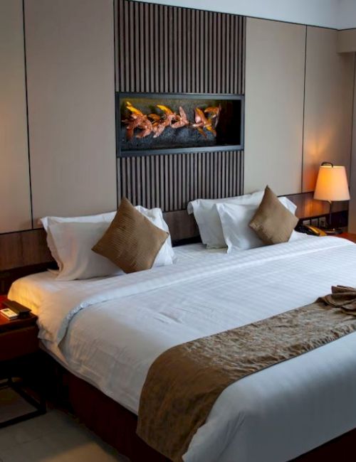 A cozy hotel room features a large bed with pillows, side tables with lamps, a decorative wall, and a curtained window.
