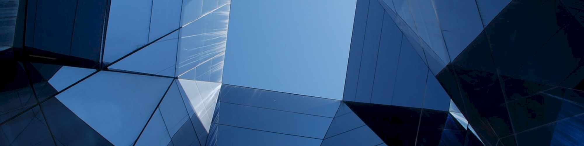 A view looking up at mirrored skyscrapers with a gap in the center revealing the blue sky, creating a geometric and abstract perspective.