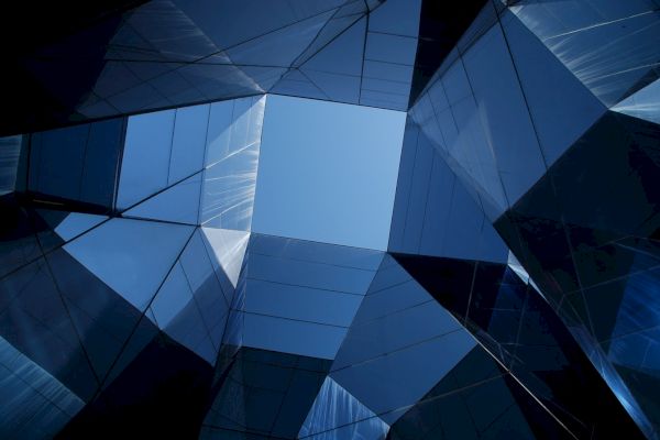 Geometric architectural structure viewed from below, creating a symmetrical pattern with a clear sky visible through the center.