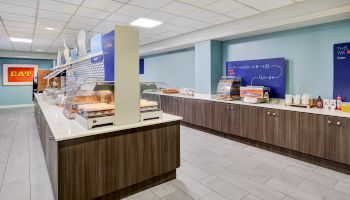 The image shows a sleek buffet area with food displays on a long counter, bright lighting, and signs.