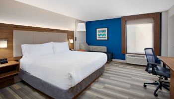 A modern hotel room with a large bed, lounge chair, desk, blue accent wall, and contemporary decor.