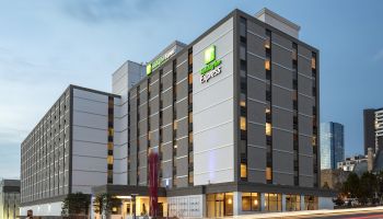 The image shows a multi-story hotel building with "Express" signage, set against a city skyline during twilight.