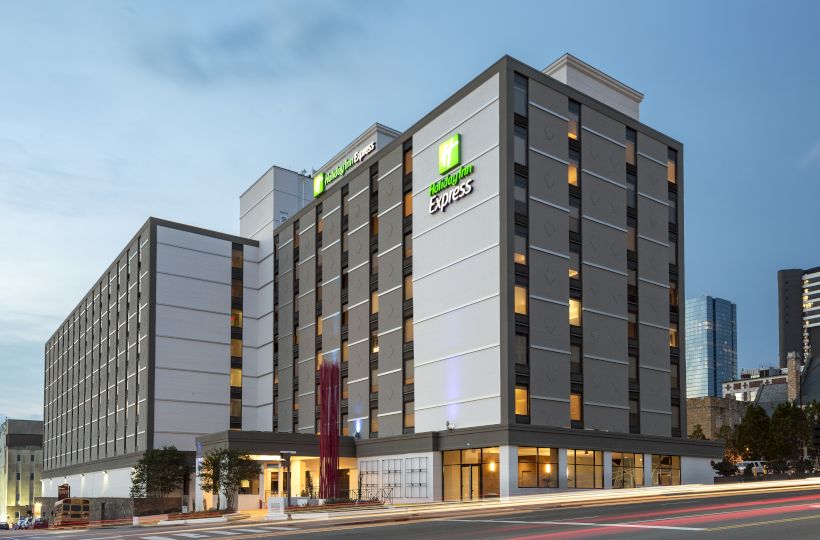 The image shows a multi-story hotel building with "Express" signage, set against a city skyline during twilight.
