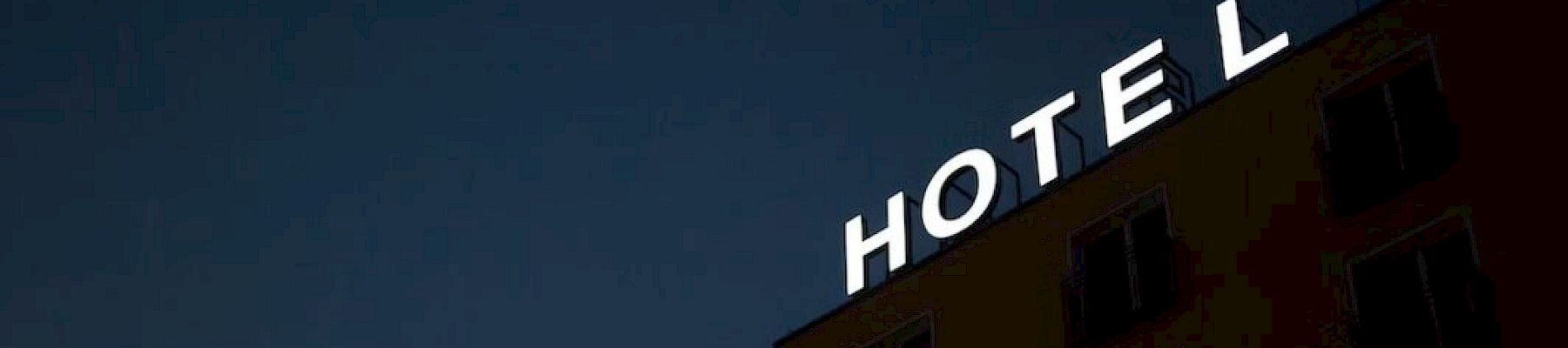 A building at night displays a bright "HOTEL" sign on its rooftop against a dark sky backdrop.