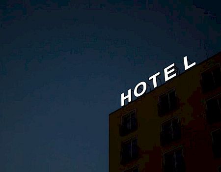 A building at night displays a bright "HOTEL" sign on its rooftop against a dark sky backdrop.