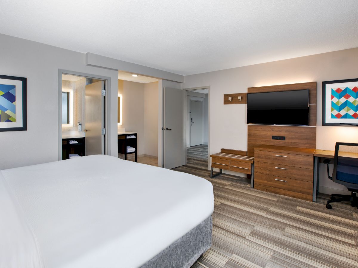 A modern hotel room features a bed, desk, TV, abstract art, and a bathroom.