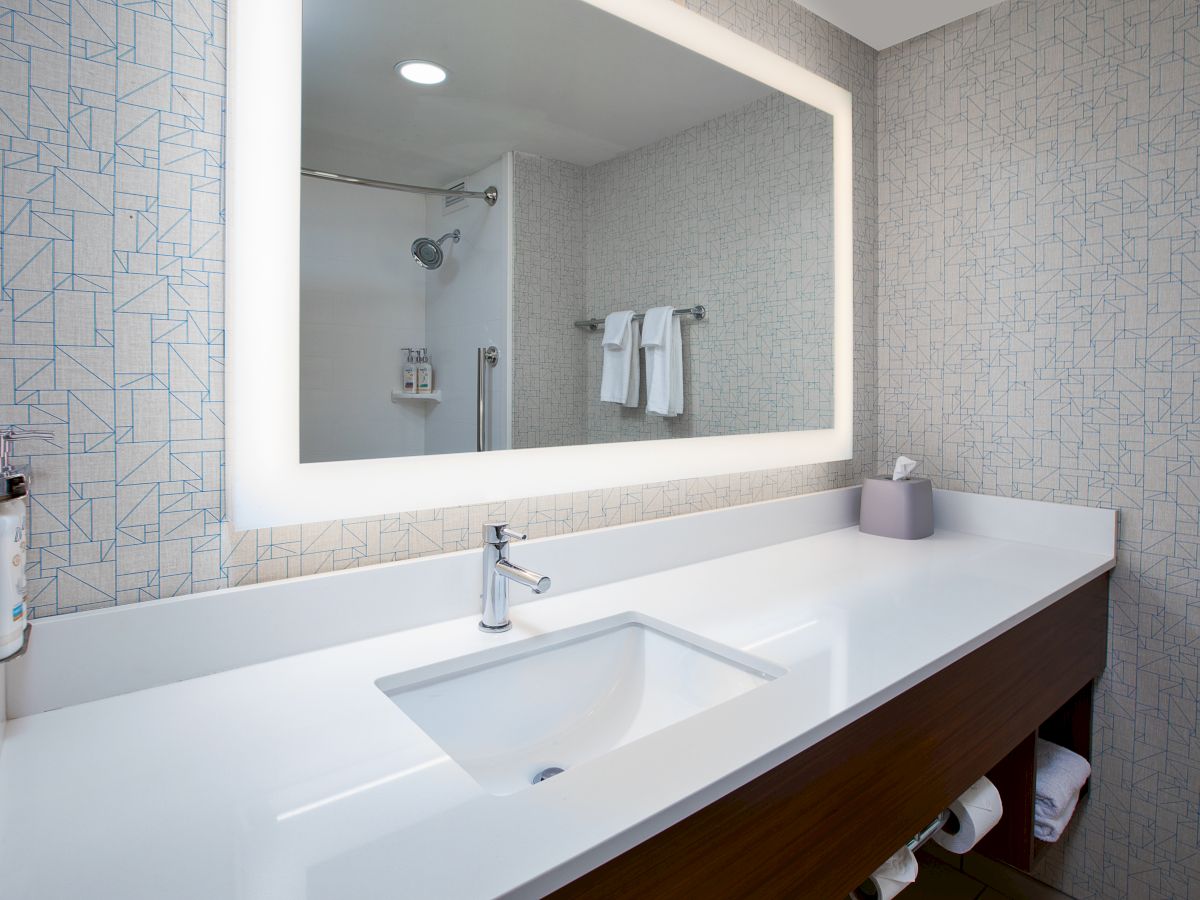 A modern bathroom with a backlit mirror, sink, countertop, and towel rack. The space is clean and minimalist in design.
