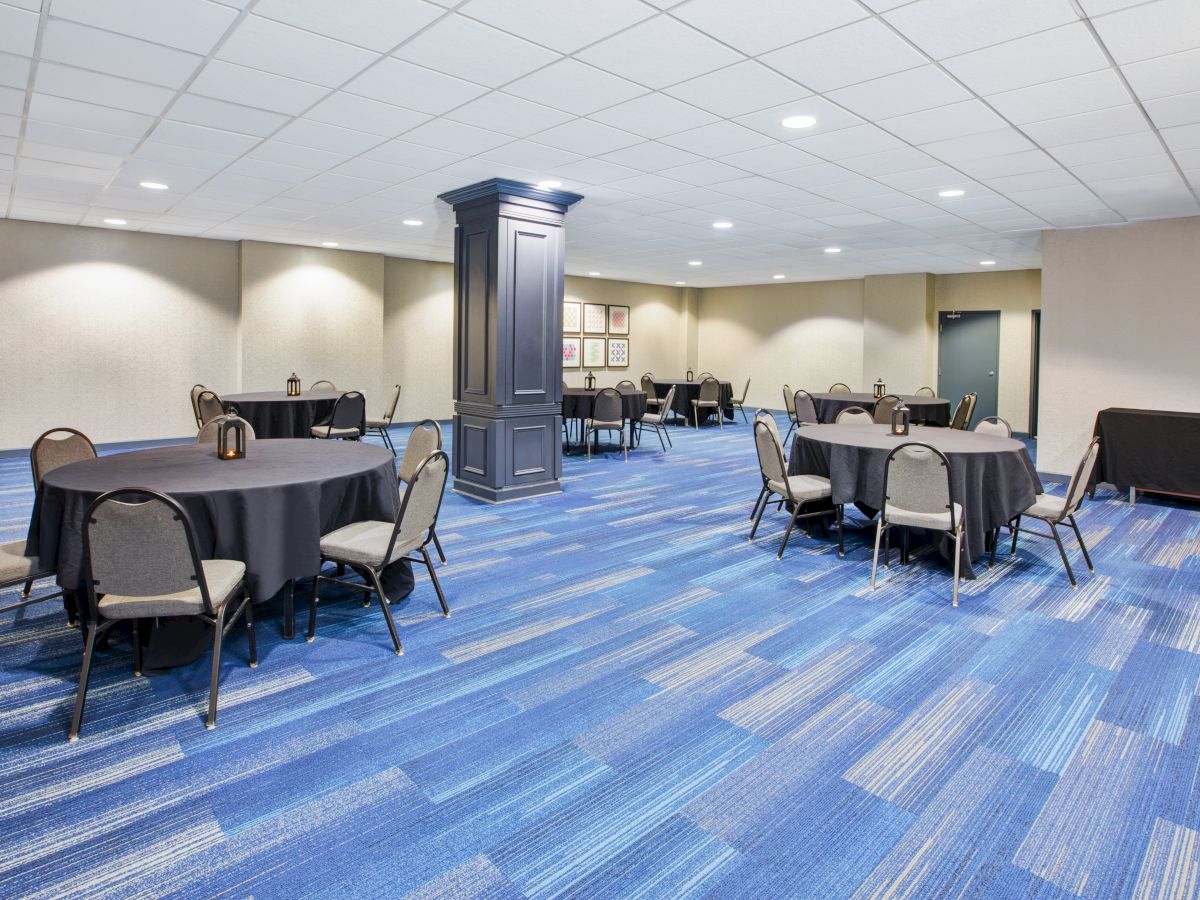 A conference room with round tables, black tablecloths, and chairs on a blue-patterned carpeted floor under a white ceiling.