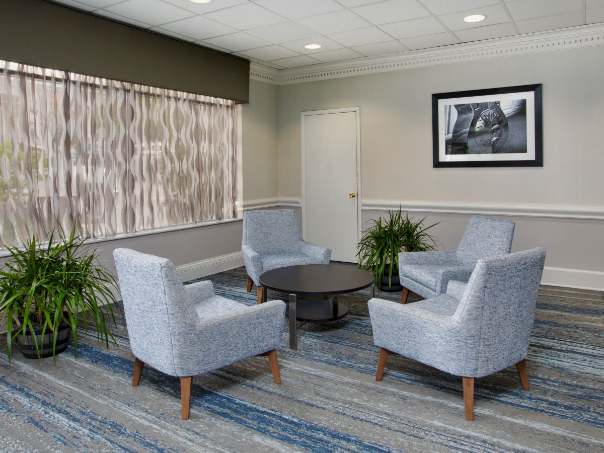 A seating area with four chairs around a table, two plants, and a black-and-white photo on the wall.