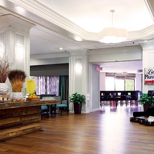 The image shows a hotel lobby with a refreshment table and a musician performing live. There are signs, decor, and seating in the background.