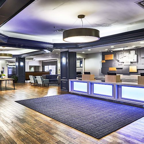 The image shows a modern hotel lobby with a stylish wooden floor, reception desk, seating area, decorative lighting, and contemporary decor.