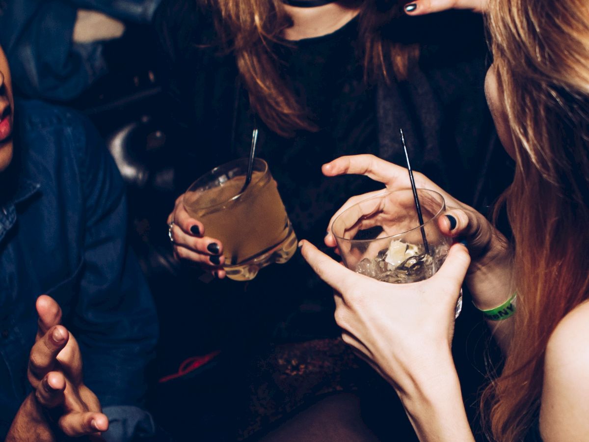 People are enjoying a lively night out, holding drinks, with one person laughing and others gesturing energetically in conversation.