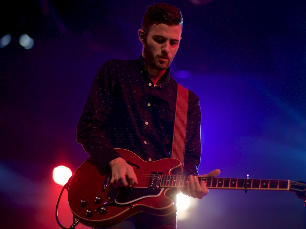A person is playing an electric guitar on stage with colorful lights illuminating the scene.