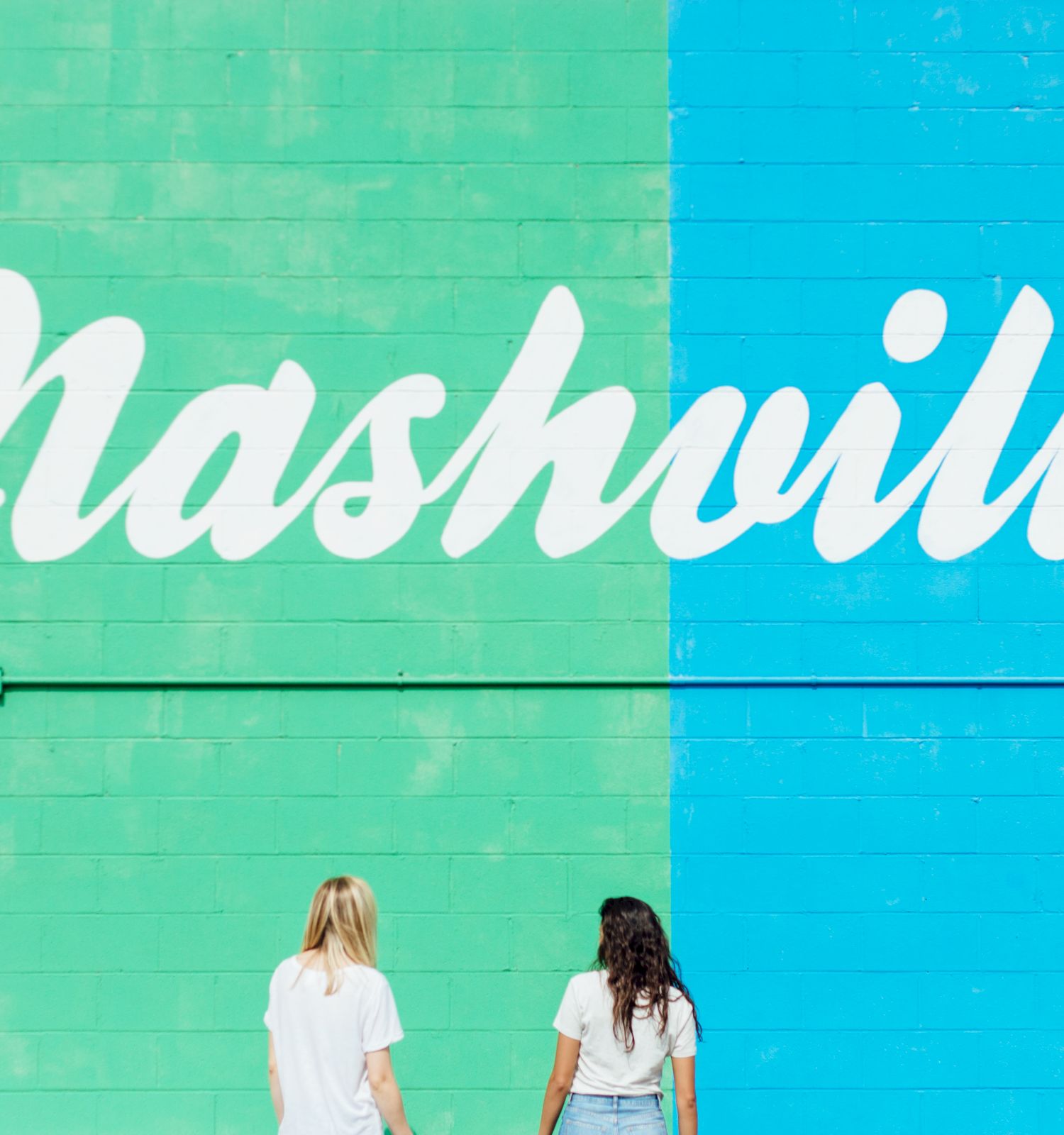 Two people stand in front of a colorful wall with the word "Nashville" written in large white letters.