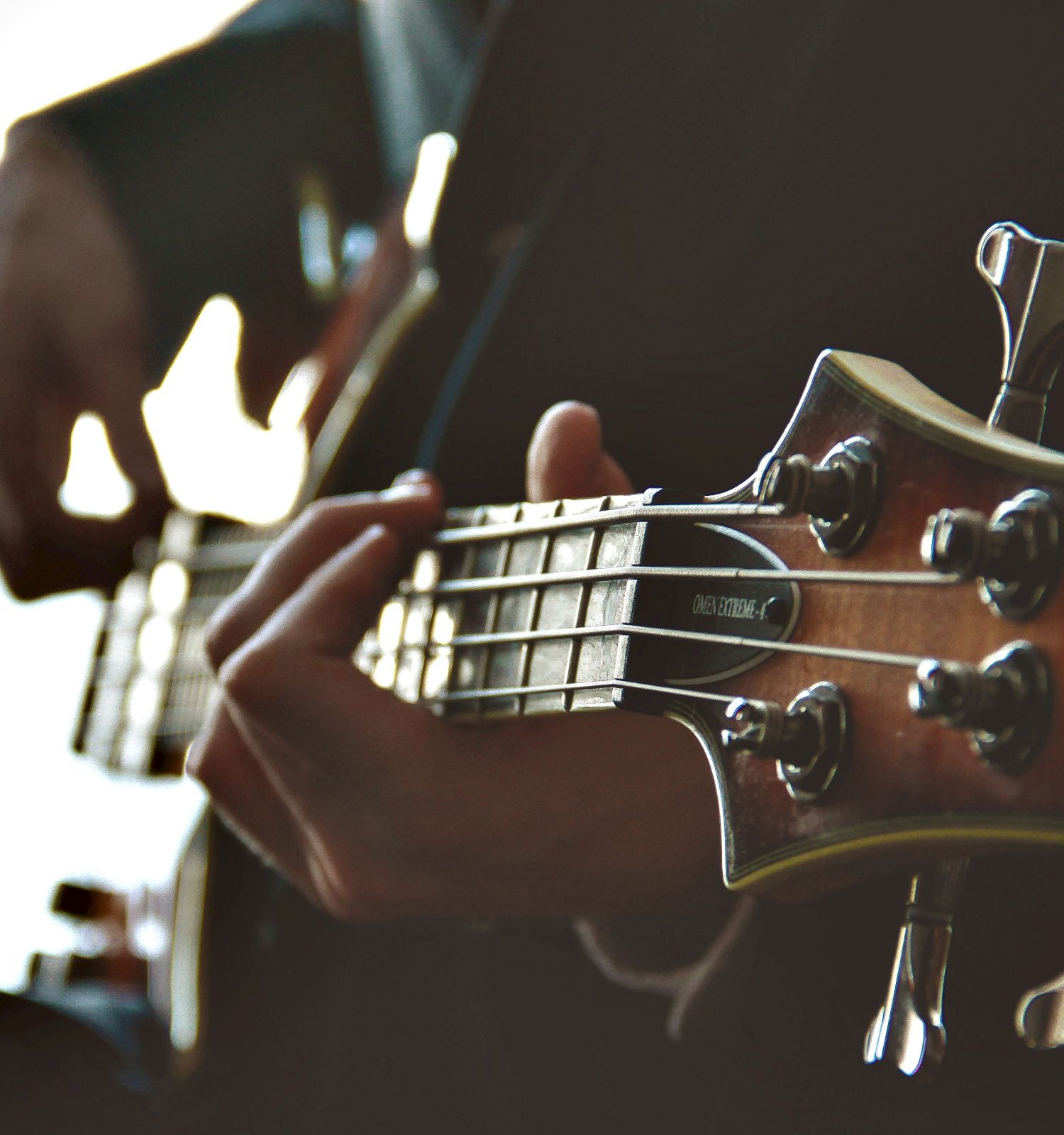 A person is playing a bass guitar, focusing on the neck and tuning pegs.