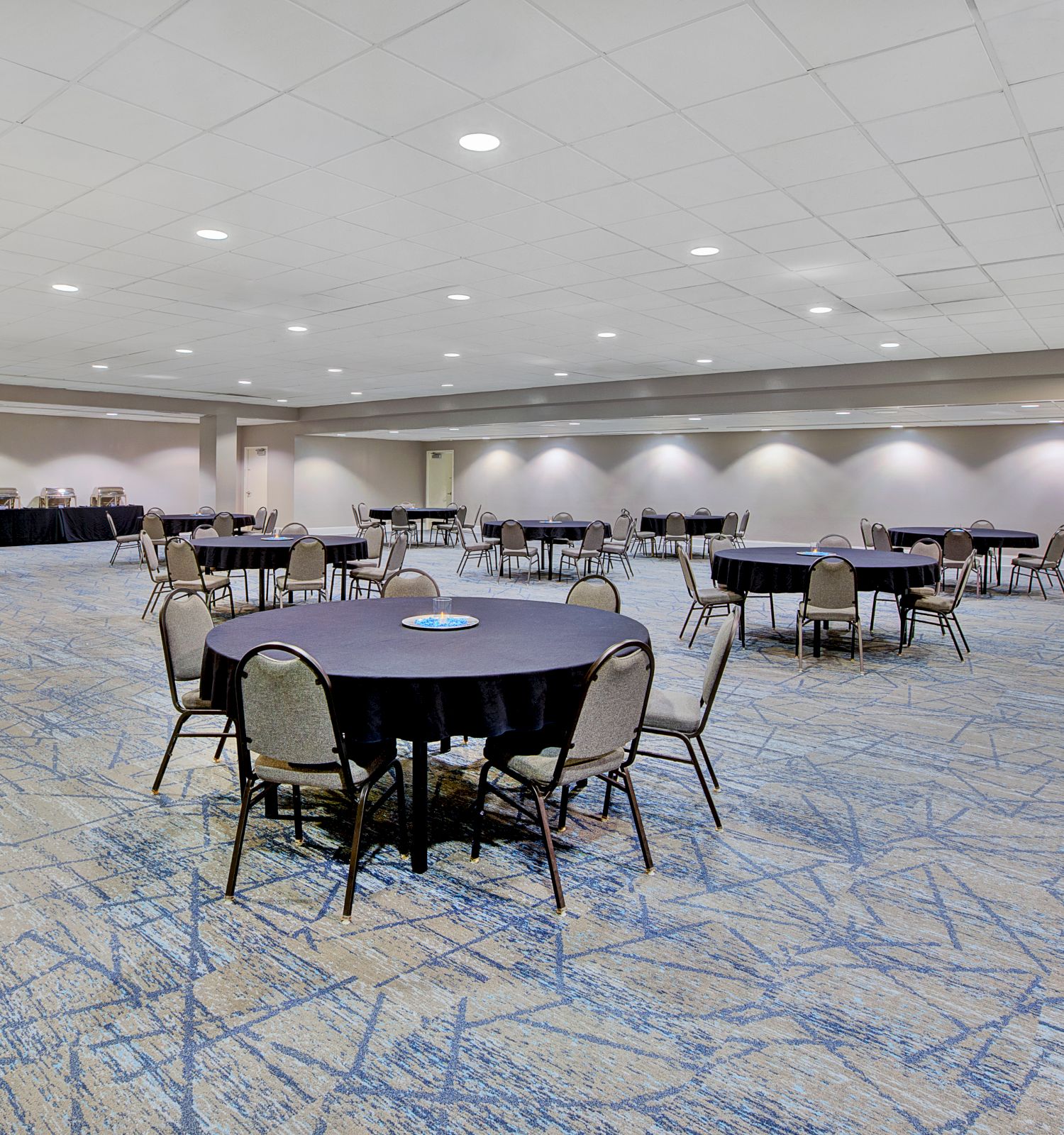 An empty conference room with round tables and chairs on a carpeted floor, ready for an event or meeting.