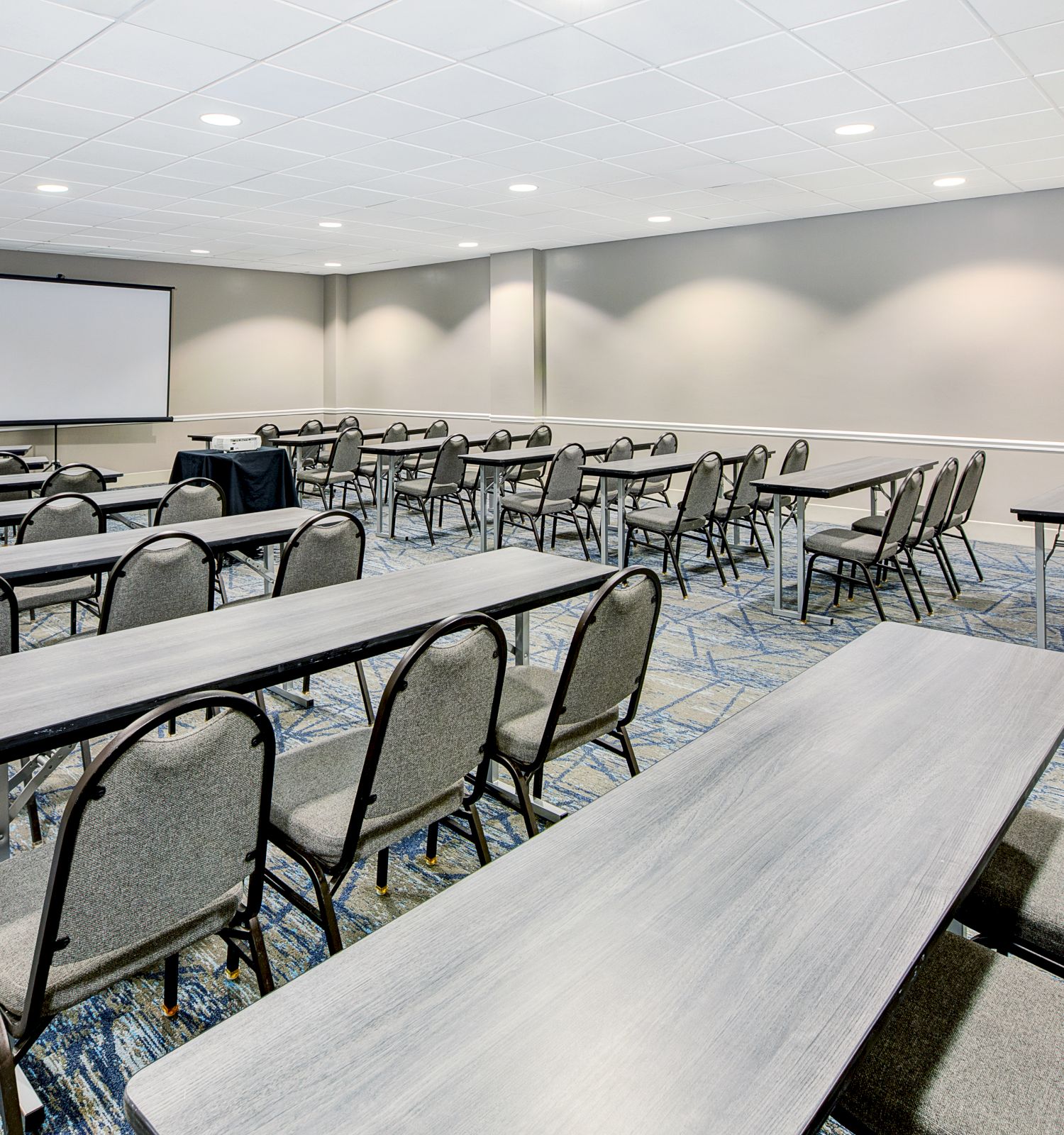 The image shows a conference room with long tables, chairs, and a projector screen on the wall, ready for a meeting or presentation.