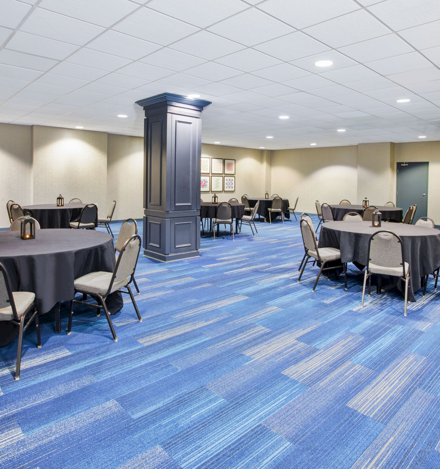 The image shows an empty conference room with blue carpet, round tables with black tablecloths, and chairs arranged around the tables.