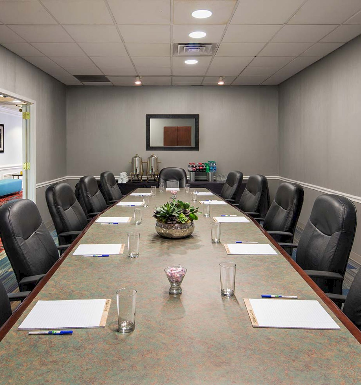A long conference table with chairs, notepads, and water glasses in a room with framed pictures on the walls.