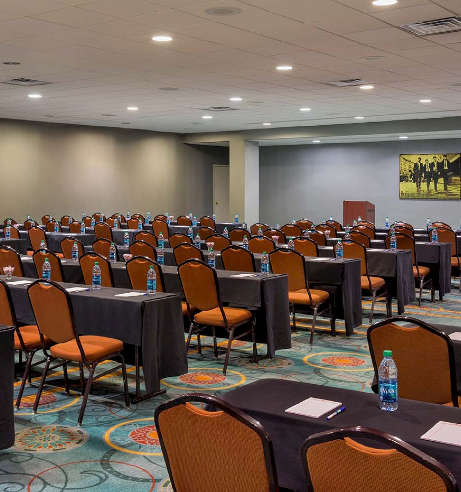 A conference room is set up with rows of tables, chairs, bottled water, and notepads, ready for an event or meeting.
