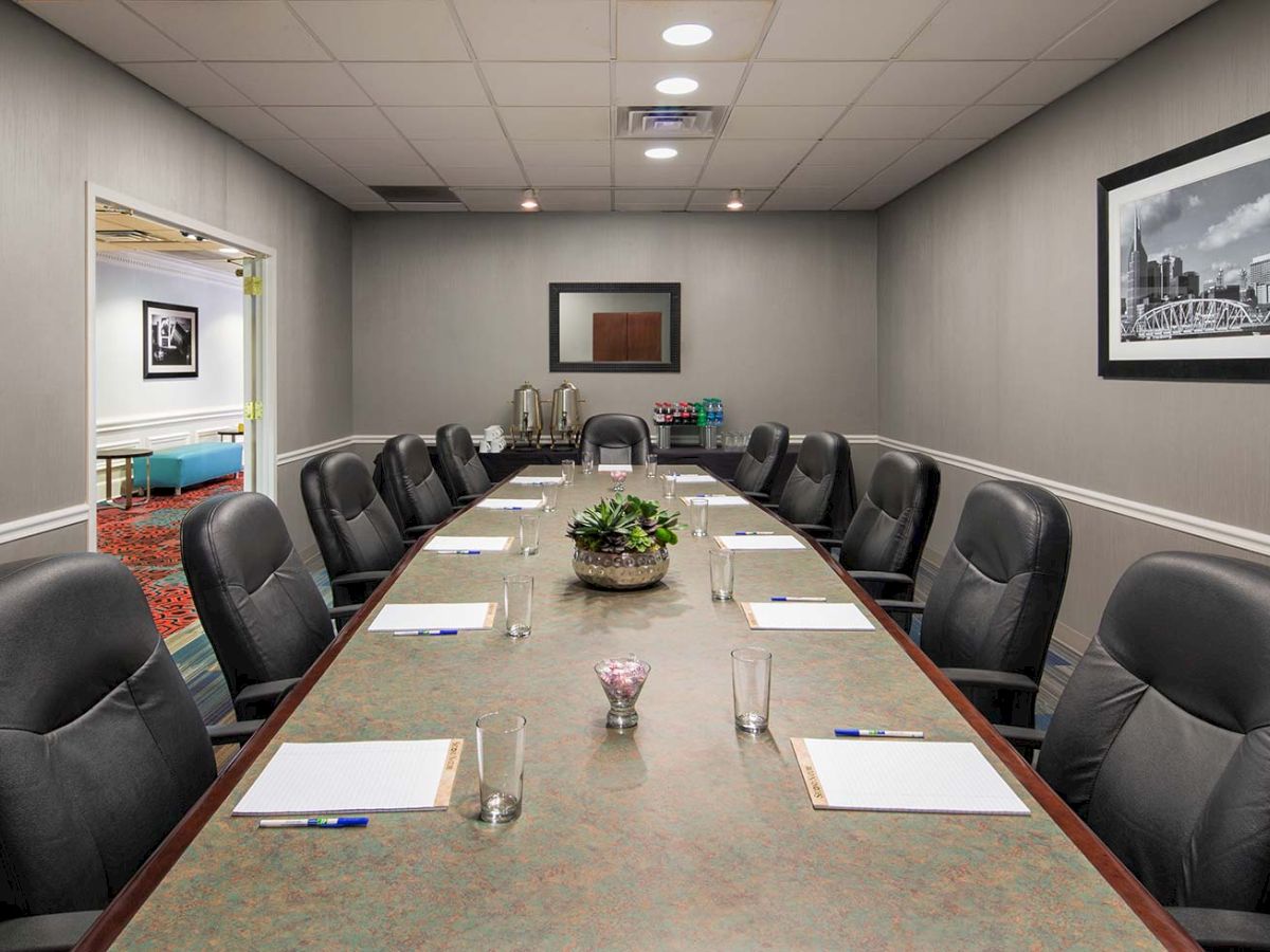 A conference room with a long table, surrounded by leather chairs, and notepads set up; artwork on walls and a plant centerpiece.
