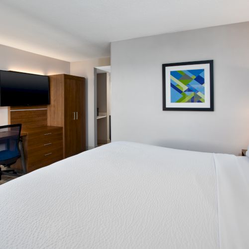 The image shows a hotel room with a bed, desk, TV, and a colorful abstract painting on the wall.