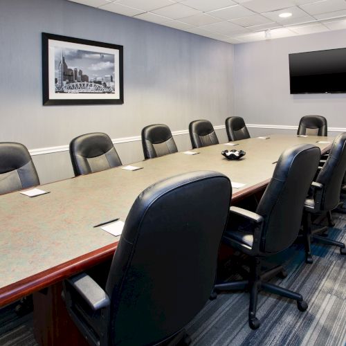 A conference room with a long table, chairs, a wall-mounted TV, and framed picture on the wall.