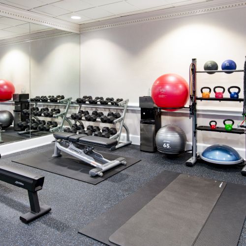 A gym with exercise equipment, including weights, kettlebells, a rowing machine, exercise balls, and mats, reflected in a mirror.
