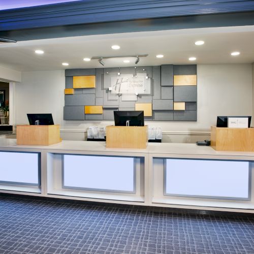 A modern hotel reception desk with computers, sleek lighting, and decorative wall panels, creating a welcoming atmosphere.