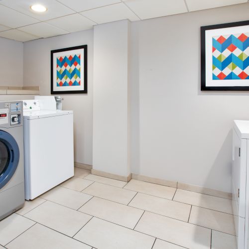 A laundry room with a washing machine, dryer, tiled floor, and colorful geometric artwork on the walls.