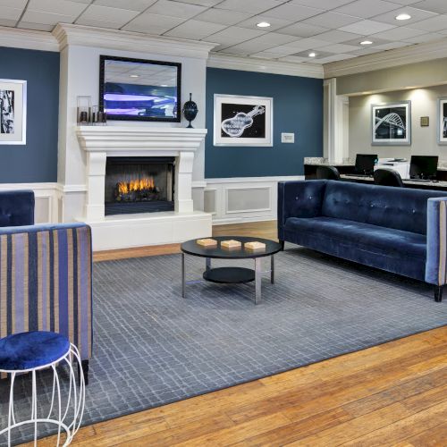 A modern lounge area with blue sofas, striped stools, a fireplace, a TV, and artwork on the walls, featuring wooden flooring.
