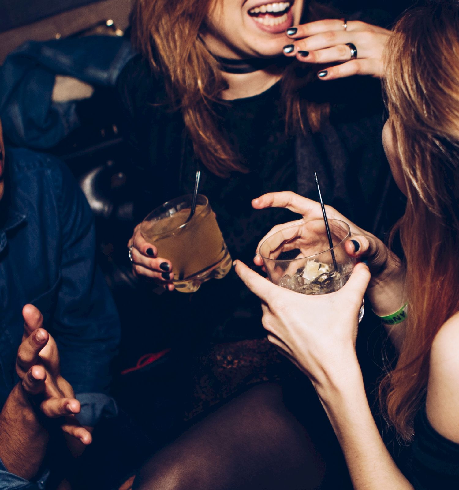People are socializing at a party, holding drinks, and engaging in lively conversation.