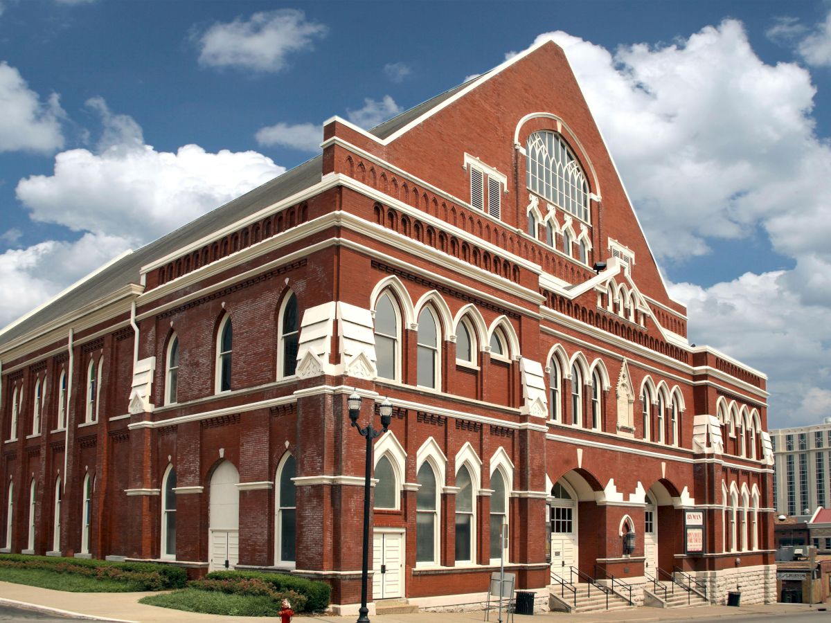 The image shows a historic red brick building with arched windows and a gabled roof under a blue sky with clouds.