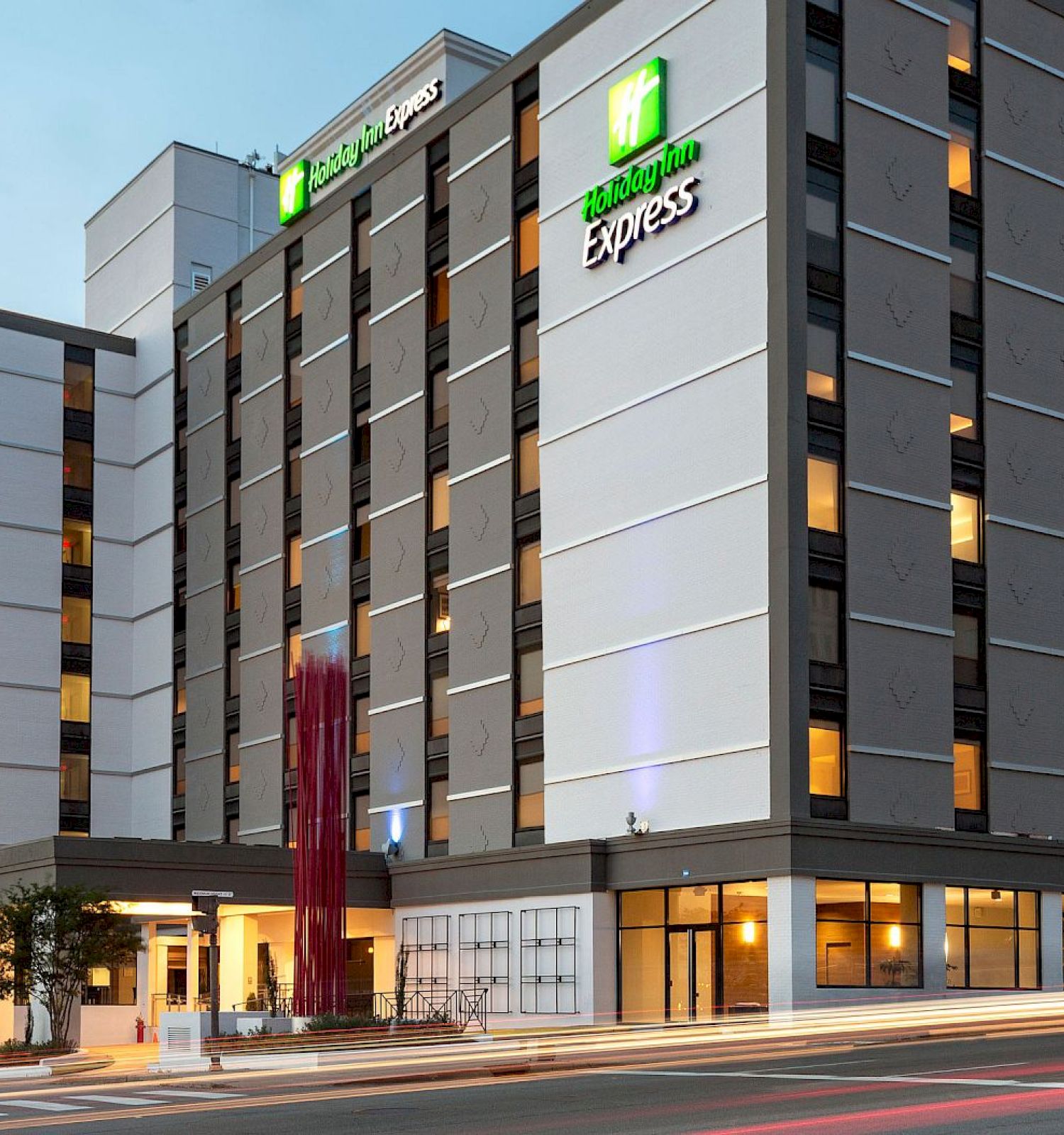The image shows a modern multi-story hotel building with a well-lit exterior and signage that reads "Holiday Inn Express."