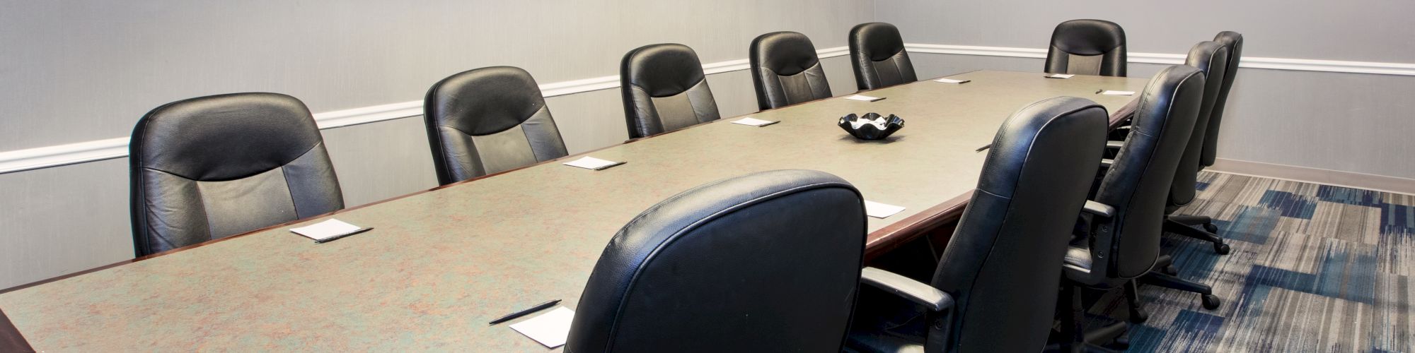 A conference room with a long table, black chairs, a wall-mounted TV, and a framed picture.