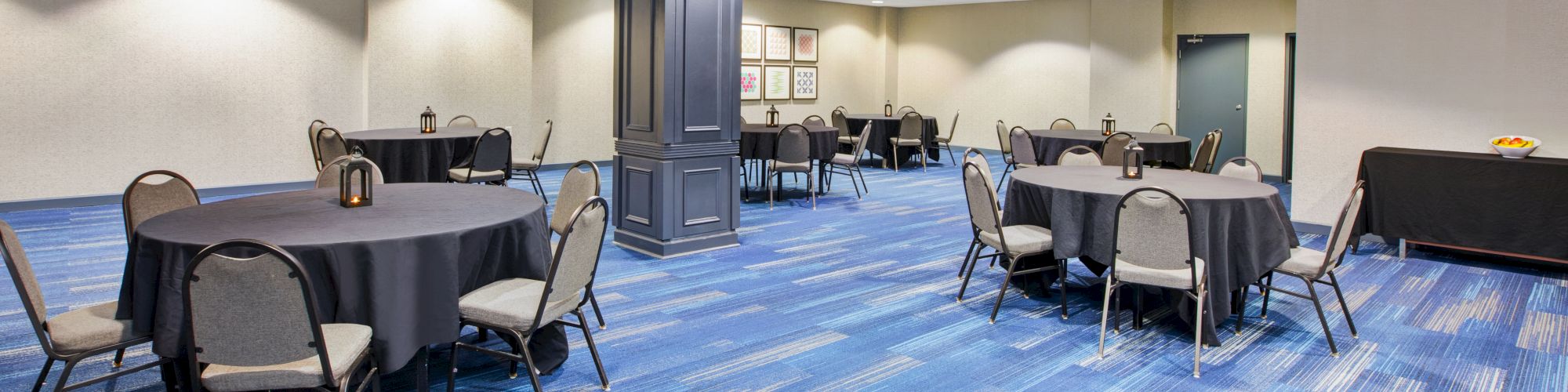 The image shows a conference room with round tables and chairs, covered in black tablecloths on a blue carpet floor.