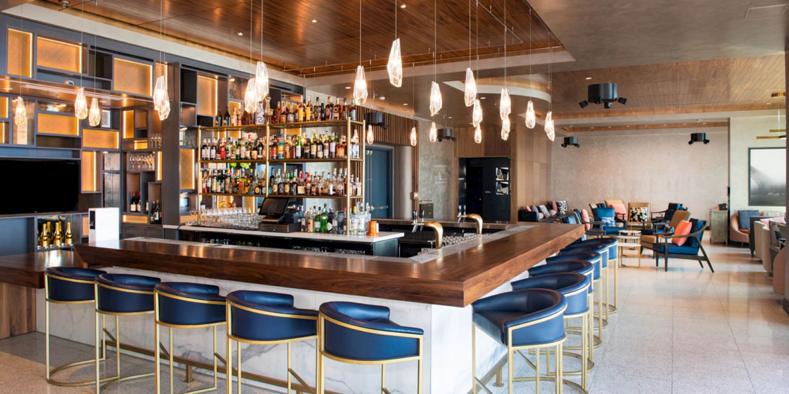 A modern bar with high chairs, a well-stocked shelf, and pendant lights provides a cozy seating area for patrons.