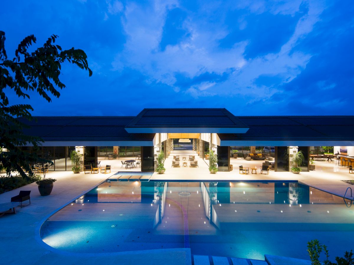 A modern building with an illuminated pool in the foreground, set against a twilight sky.
