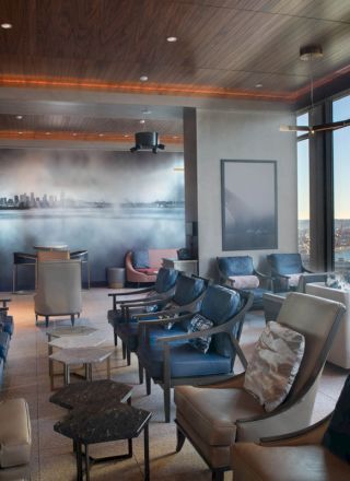 A modern, upscale lounge with comfortable seating, large windows offering a scenic ocean view, and a mural on one wall.