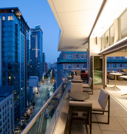 A modern rooftop patio with outdoor seating overlooks a city street lined with tall buildings, captured during the evening.