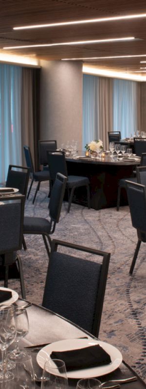 The image shows an elegant banquet hall with round tables set for a formal event, featuring dark chairs and dim lighting.
