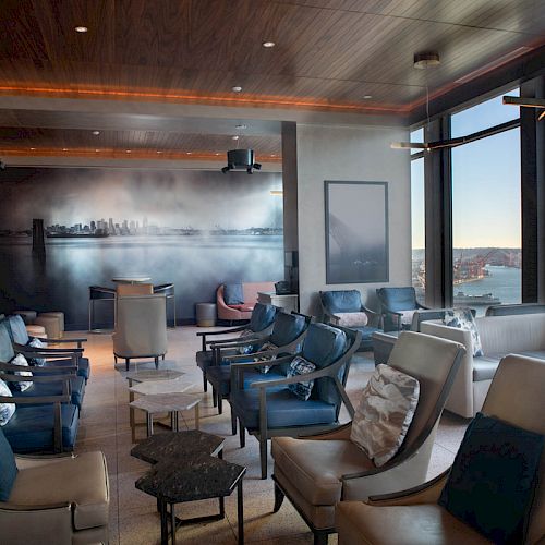 A modern lounge with plush seating, wall art, and large windows offering a scenic waterfront view, featuring calm and elegant décor.