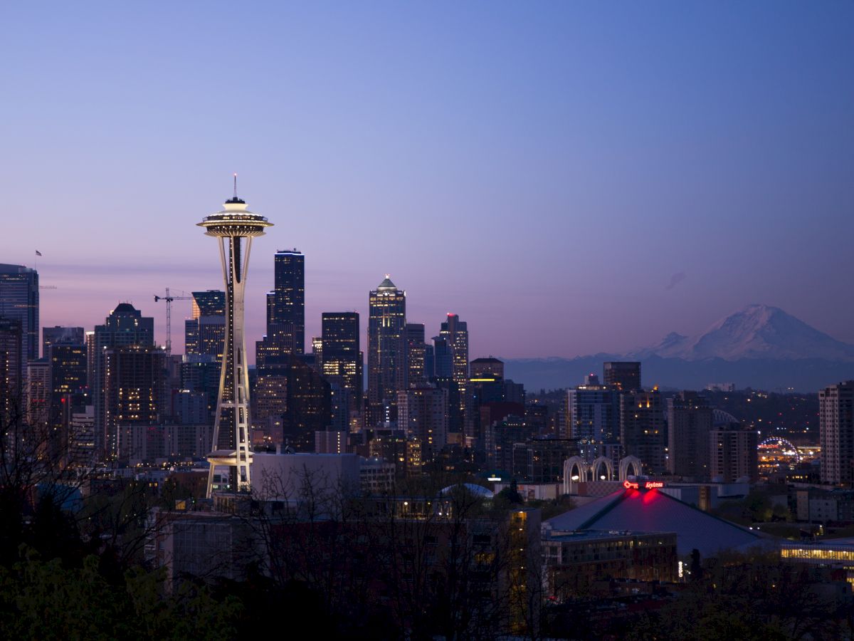 The image shows a city skyline at dusk with the Space Needle, skyscrapers, and a mountain in the background under a blue and purple sky.
