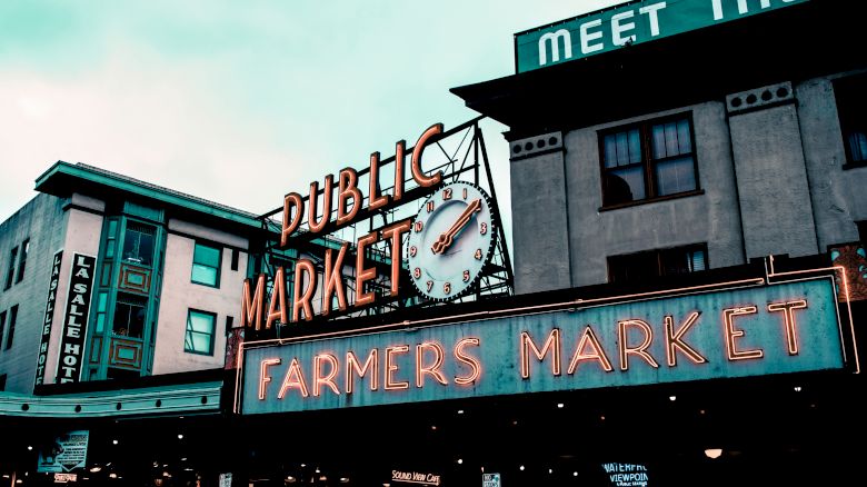 The image shows the iconic entrance signs for a public market and farmers market, with a visible clock and neon lettering.